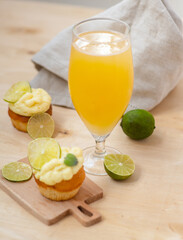 A glass of light beer stands next to a lime cupcake dessert on a light wooden background