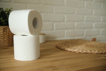 Toilet paper on a wooden table. Two white rolls. Brick background. A green flower. White and beige colors