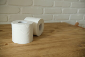 Toilet paper on a wooden table. Two white rolls. Beige colors. White brick wall in the background