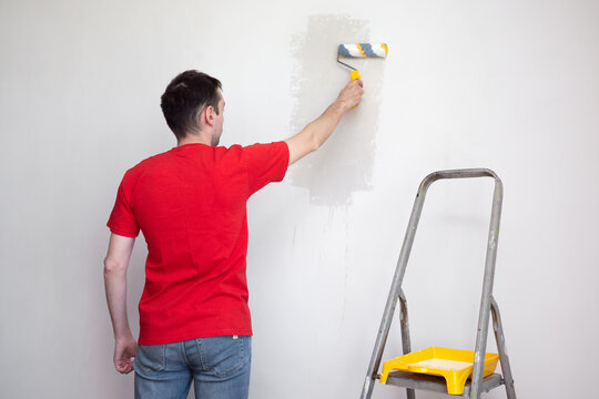 Man priming the wall with a roller. Repair of the interior. Young male decorator painting a wall in the empty room. Concept renovation do it yourself.