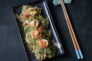 Yakisoba, green tea noodle stir fry with prawns on black background, flat lay