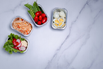Take away healthy food in foil boxes on marble table. Copy space