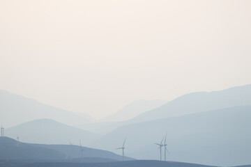 Fototapeta na wymiar Mountains silhouette in the morning haze, wind turbines on the top, copy space, Greece