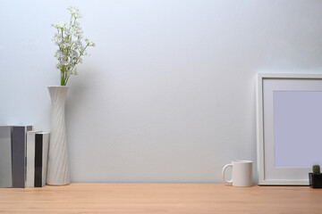 Modern workplace with white picture frame, books and coffee cup on wooden table.
