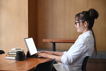 Young asian woman sitting in library and surfing internet with computer tablet.