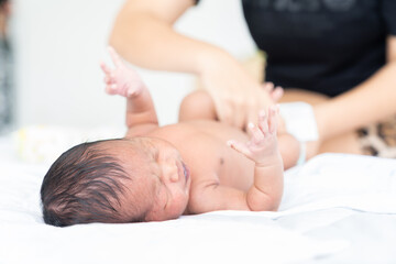 Mom wiping her newborn baby skin, face with wet wipes carefully on bed at home. family, cleaning wipe and infant concept