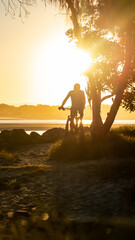 Obraz na płótnie Canvas Silhouette of Man Ride a Bicycle at the Coast in Summer at Sunset Background in Noosa, Australia