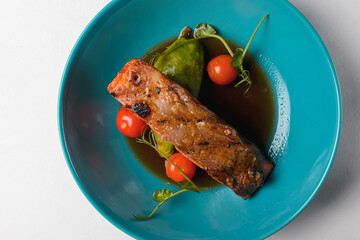 Fish steak with cherry tomatoes and soy sauce served in a blue bowl over white background.