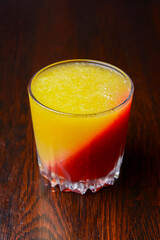 A colorful treat of layered gelatin dessert. Fruit jello red and yellow in a small glass on a wooden table.