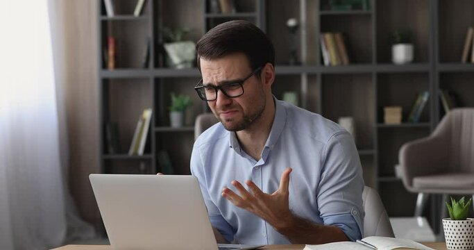 Bad-tempered man sit at desk stressing out while work on laptop, having difficulties with device, blogger read unpleasant comment text rude answer to subscriber, modern tech, nervous breakdown concept