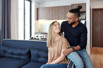 Portrait of joyful young beautiful couple sitting on sofa at home and looking at each other