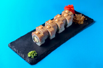 Japanese sushi with eel, wasabi sauce and pickled ginger served on a black board over blue background.