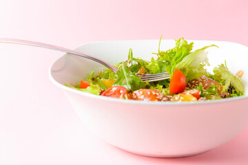 Fresh salad with salmon and vegetables close up in a bowl over pastel pink background.