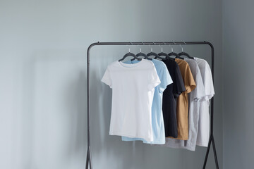 T-shirts of neutral colors on  black hanger against  gray wall