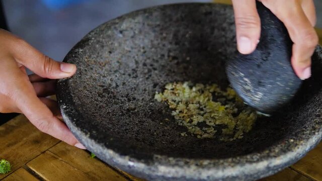 Female hand crushing garlics using stone pestle and mortar. Crushed garlic in stone mortar in close up