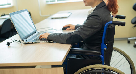 Young woman works at a laptop while sitting in a wheelchair in a university lecture hall. Conditions for teaching a disabled person