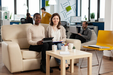 Start up company teamwork talking during video meeting sitting on couch listening and explaning to remote manager team strategy. Multiethnic coworkers discussing about startup financial project.