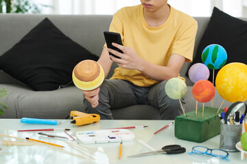 Teenage boy phototgraphing model of Jupiter planet he made out of styrofoam ball for school project © DragonImages