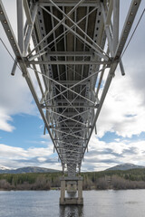 Below the magnificent Johnsons Crossing Bridge over Teslin River in northern Canada during spring, summer time with steel beams running above and blue sky in background. 