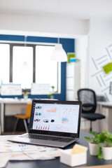Close up of laptop in start up company office with charts and statistics. Brainstorm area in business center with nobody in it, shot of empty room with modern furniture and blue wall.
