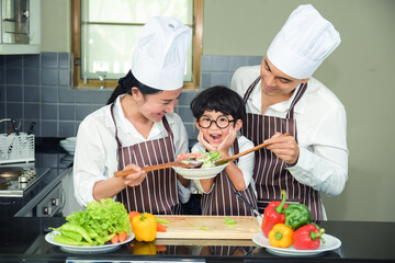 Asian woman young mother with son boy cooking salad food with vegetable holding tomatoes and carrots, bell peppers on plate for happy family cook food enjoyment lifestyle kitchen in home