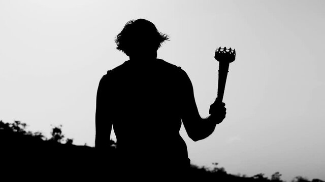 Back view silhouette shot of athlete climbing mountain by holding Olympic torch