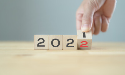 Businessman hand holding wooden cube with flip over block years 2021 to 2022 Plans word on table background. Resolution, strategy, solution, goal, action plan, business and new year holiday concepts