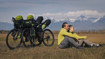 The man and woman travel on mixed terrain cycle touring with bikepacking. The two people journey with bicycle bags. Sport bikepacking, bike, sportswear in green black colors. Mountain snow capped.
