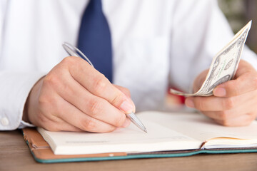 Man jot down things and some dollar banknotes in his notebook