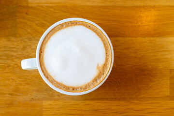 Beautiful surface of hot latte coffee in a cup from top view served on the wooden table. Photograph of latte coffee from top view on wooden table close up.