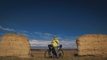 The man travel on mixed terrain cycle touring with bikepacking. The traveler journey with bicycle bags. Sport bikepacking, bike, sportswear in green black colors. Mountain snow capped, stone arch.