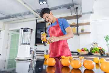 Healthy handsome man with casual clothes is smiling and preparing orange juice to diet, in kitchen at home in holiday.