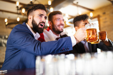 Men fans screaming and watching football on TV and drink beer in a pub