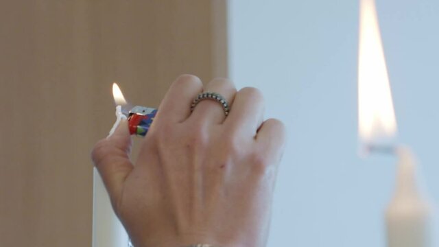 Close-up of girl's hand lighting a candle. A woman uses a lighter to light a couple of candles for the dining table.