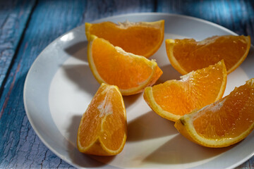 Fototapeta na wymiar Close-up of an orange cut into wedges, on a plate on a blue table.