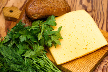 a piece of cheese greens and two rye buns on a cutting board on the wooden table of the village collection. Organic food. Organic product.