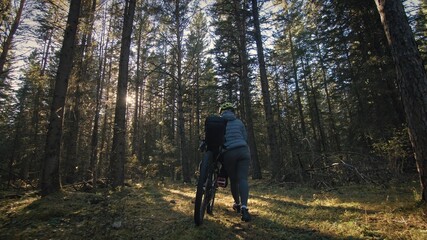 The woman travel on mixed terrain cycle touring with bike bikepacking outdoor. The traveler journey with bicycle bags. Stylish bikepacking, bike, sportswear in green black colors. Magic forest park.