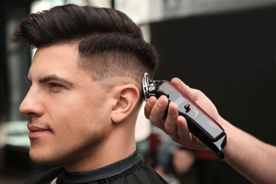 Professional barber making stylish haircut in salon, closeup