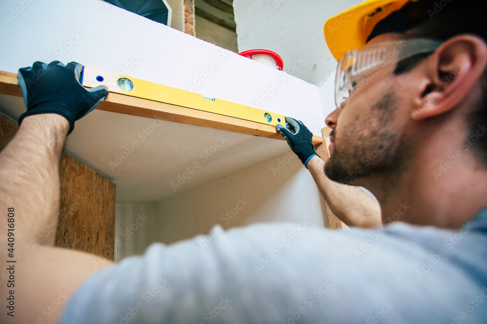 Wall mural young home repair male or worker busy with house renovation, holds building equipment, wears casual 