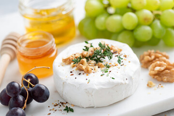 Camembert cheese served with walnuts, grapes and honey. Closeup view. Gourmet white cheese
