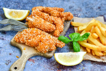 
 Crispy  deep fried   chicken strips  with sesame seeds and french fries . Breaded  with cornflakes chicken  breast fillets  with chilly peppers and fresh   basil on wooden rustic background