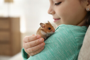 Little girl holding cute hamster at home, closeup