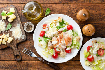 Caesar salad with grilled chicken breast, cherry tomatoes and sauce on a wooden table background, top view