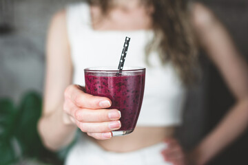 Purple acai smoothie in female hands. Unrecognizable young fitness girl holding glass of superfood purple smoothie