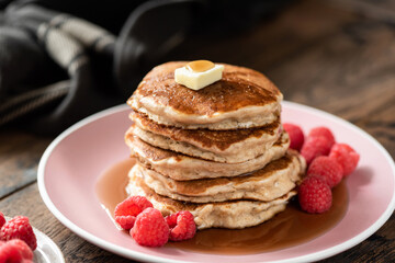Healthy oat pancakes with raspberries and maple syrup on a pink plate, wooden table background