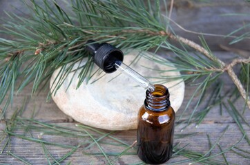 glass bottle of essential oil with a dropper on a stone with a wooden background with pine branch and cones