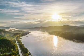 sunset on the river, evening sun illuminates the hills and the road along the river, aerial view
