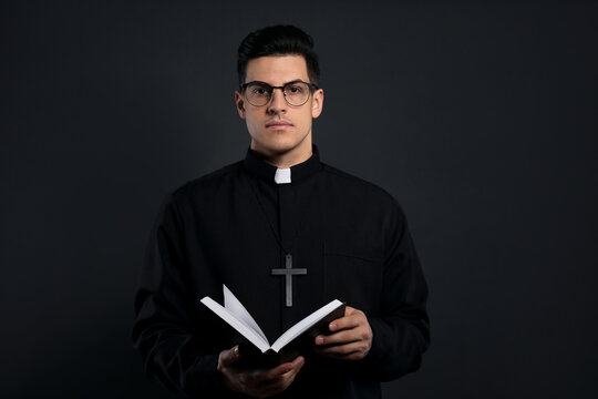 Priest In Cassock With Bible On Black Background