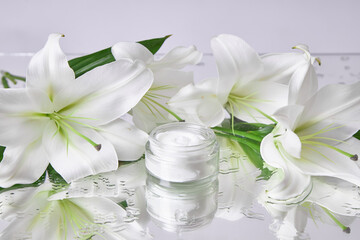 Fototapeta na wymiar Cream for skin care, natural cosmetics made of flowers and petals. A glass jar of white cream stands among the lily flowers