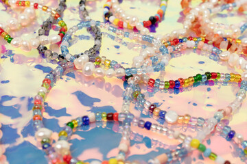 Closeup of necklaces and bracelets made from colorful beads and pearls on a pink holographic...